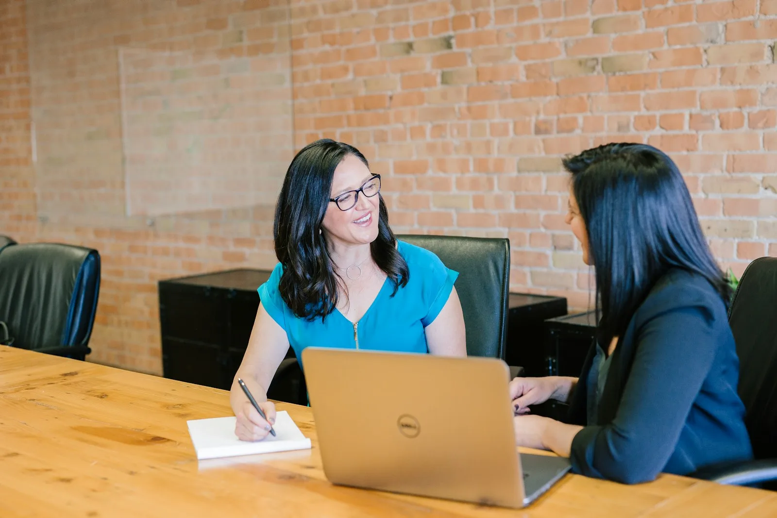 Dos mujeres latinas revisan una computadora en una oficina y conversan con atención y calma